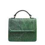 Dark green handbag with stunning leaf grain throughout the exterior. The bag features a dark green handle with chrome attachment hardware. The front opening features a flat double stitched fold with beveled corners. Inside the bag features a chrome zippered interior pocket. This bag is also offered in an electric blue variant with a smooth black interior and the same beautiful exterior leaf grain. Both variants may come with a color matched modular shoulder strap.